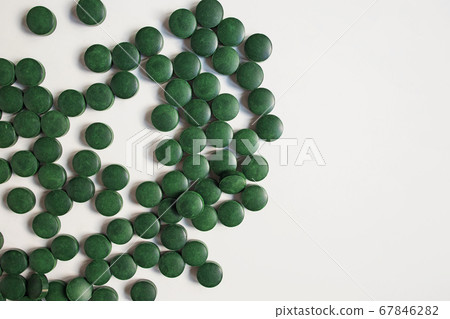 Green pills on wooden scoop isolated on white background with reflection. Spirulina, chlorella and wheatgrass. Healthy living concept. Green pills on wooden scoop isolated on white background with reflection. Spirulina, chlorella and wheatgrass. Healthy living concept. 67846282