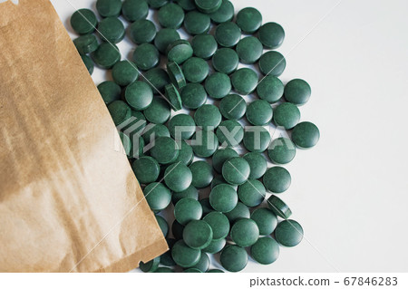 Green pills on wooden scoop isolated on white background with reflection. Spirulina, chlorella and wheatgrass. Healthy living concept. Green pills on wooden scoop isolated on white background with reflection. Spirulina, chlorella and wheatgrass. Healthy living concept. 67846283