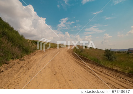 Scenic beautiful nature with green grass and dramatic cloudy sky in hot summer day. Yellow sandy road and spirit of adventures, mountains on a background 67848687