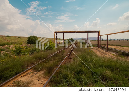 Soligork salt mine slagheap mountains and scenic beautiful nature with green grass and dramatic cloudy sky in hot summer day. Old rusty railway path and industrial metal constructions, pipes 67848694