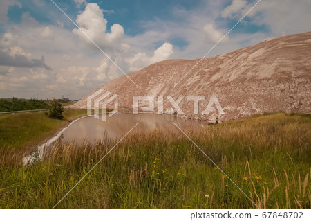 Soligork salt mine slagheap mountains and scenic nature with green grass and dramatic cloudy sky in summer day. A technical water lake and white salt rock Soligork salt mine slagheap mountains and scenic nature with green grass and dramatic cloudy sky in summer day. A technical water lake and white salt rock 67848702