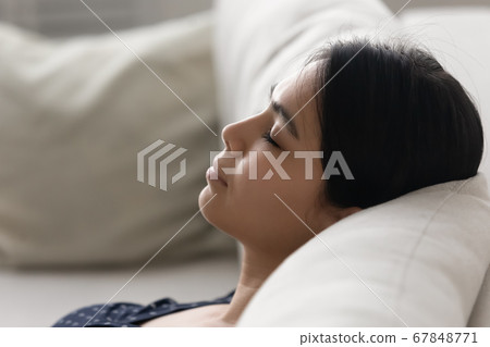 Calm Vietnamese girl relaxing on couch daydreaming 67848771