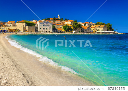 Sandy beach with waves and Primosten resort in background, Croatia 67850155