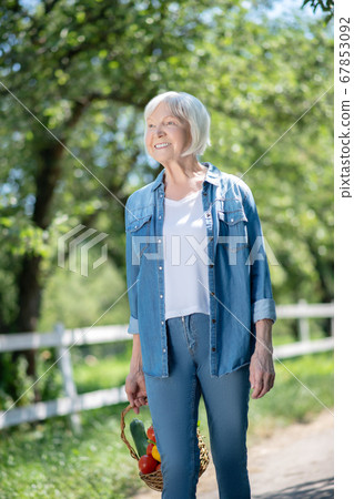 Relaxed woman wearing a denim jacket walking in a garden Relaxed woman wearing a denim jacket walking in a garden 67853092