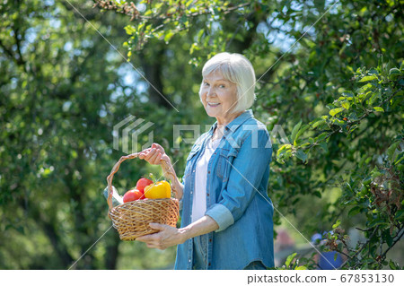 Smiling woman holding a basket with peppers and tomatoes 67853130