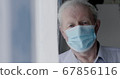 Portrait of sad grandfather in medical mask looks at camera anxiously at home 67856116