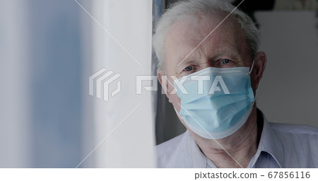 Portrait of sad grandfather in medical mask looks at camera anxiously at home 67856116