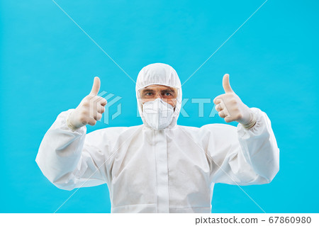 Doctor in protective medical suit showing thumbs up on blue background Doctor in protective medical suit showing thumbs up on blue background 67860980