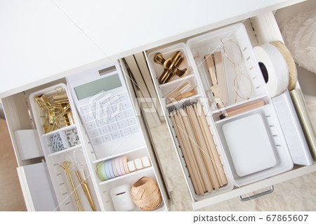 The gold stationery is neatly arranged in white containers in the drawers of the nightstand. Storage and tidying up the workplace. 67865607