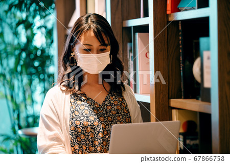 Young woman in mask working desk in front of bookshelf in office 67866758