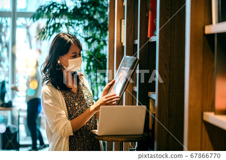 Young woman in mask working desk in front of bookshelf in office 67866770