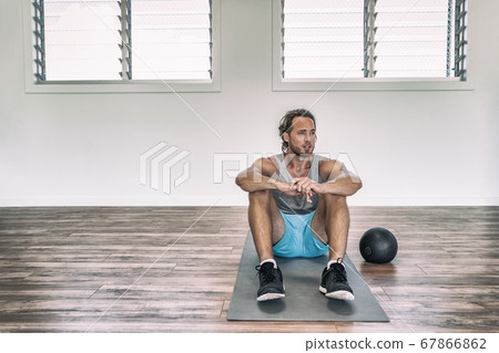 Gym workout man training floor exercises with weighted slam ball or medicine ball taking a break tired sweating thinking of disappointment Gym workout man training floor exercises with weighted slam ball or medicine ball taking a break tired sweating thinking of disappointment 67866862