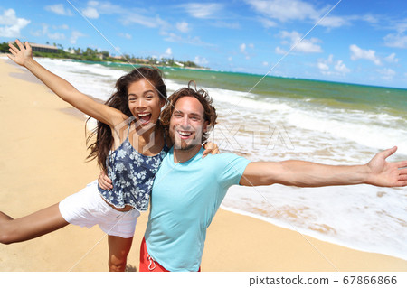 Happy people jumping screaming of fun on beach summer vacation travel in Hawaii. Laughing young Asian woman with Caucasian man, tourists couple friends on holiday 67866866