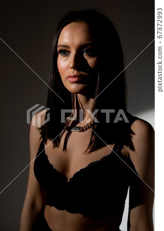 Studio photo of pretty brunette woman in twilight in bra looks into the distance 67872993