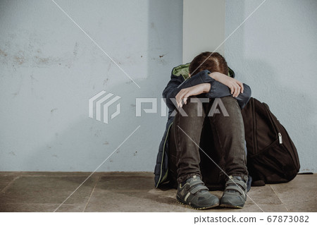 Little boy or school child sitting alone on floor in front of the school after suffering an act of bullying 67873082