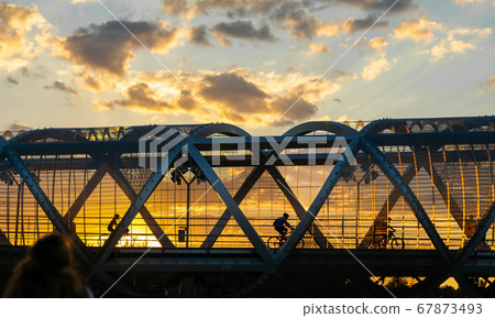 Cylists cross the bridge in the evening, sunset time , Arganzuela Footbridge, Puente de Arganzuela in Madrid Cylists cross the bridge in the evening, sunset time , Arganzuela Footbridge, Puente de Arganzuela in Madrid 67873493