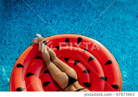 Sexy woman relax in pool laying on inflatable pool toy watermelon 67873663