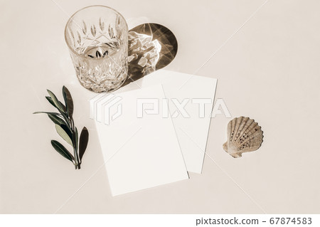 Summer still life. Glass of water, cocktail with long shadows, sea shellt and olive tree branch on beige table background in sunlight. Blank greeting card mockup. Flat lay, top view. Birthday concept. Summer still life. Glass of water, cocktail with long shadows, sea shellt and olive tree branch on beige table background in sunlight. Blank greeting card mockup. Flat lay, top view. Birthday concept. 67874583