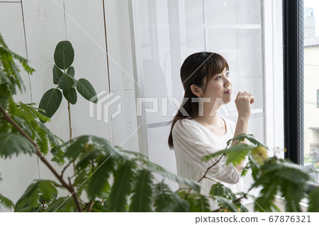 Young woman brushing teeth while looking out by the window 67876321