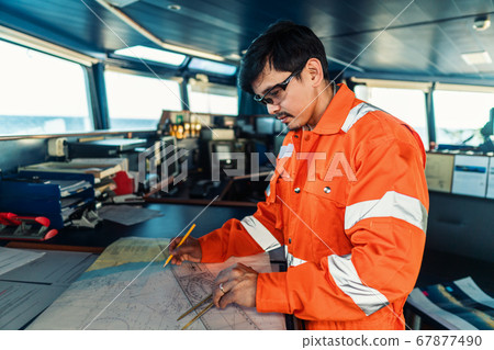 Filipino deck Officer on bridge of vessel or ship. He is plotting position on chart Filipino deck Officer on bridge of vessel or ship. He is plotting position on chart 67877490