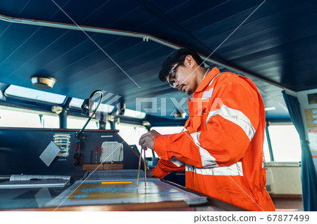 Filipino deck Officer on bridge of vessel or ship. He is plotting position on chart 67877499