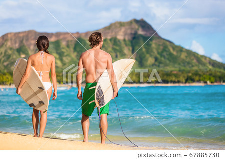 Hawaii surfers people relaxing on waikiki beach with surfboards looking at waves in Honolulu, Hawaii. Healthy active lifestyle fitness couple at sunset with diamond head mountain in the background Hawaii surfers people relaxing on waikiki beach with surfboards looking at waves in Honolulu, Hawaii. Healthy active lifestyle fitness couple at sunset with diamond head mountain in the background 67885730