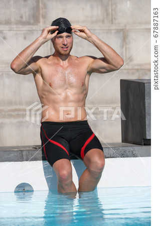 Swimmer athlete getting ready preparing for race putting on goggles glasses and cap for swim race competition at indoor swimming pool stadium. Young man in shorts his 20s Swimmer athlete getting ready preparing for race putting on goggles glasses and cap for swim race competition at indoor swimming pool stadium. Young man in shorts his 20s 67887163