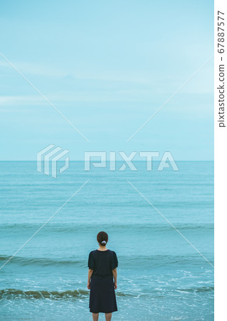 A woman standing on the edge of the beach 67887577