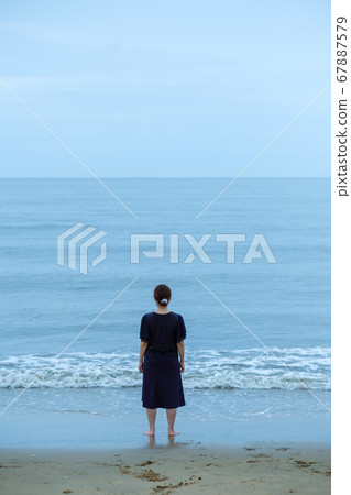 A woman standing on the edge of the beach 67887579
