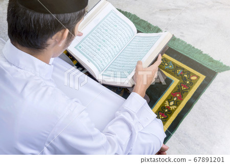 Asian Muslim man sitting and reading the Quran Asian Muslim man sitting and reading the Quran 67891201