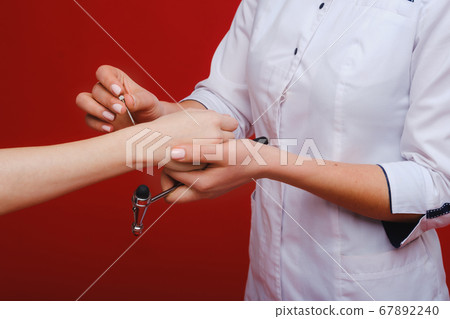 The doctor is holding a neurological hammer on a red background. The neurologist checks the patient's reflexes with a hammer. Diagnostics, healthcare, and medical care The doctor is holding a neurological hammer on a red background. The neurologist checks the patient's reflexes with a hammer. Diagnostics, healthcare, and medical care 67892240