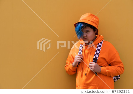 Back to school. A teenage girl with blue hair in an orange hoodie, a Panama hat with a backpack. A high school kid. 67892331