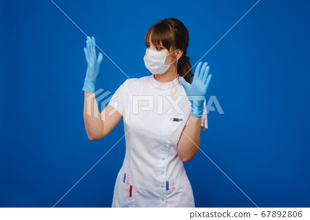 A girl doctor stands in a medical mask, isolated on a blue background. A girl doctor stands in a medical mask, isolated on a blue background. 67892806