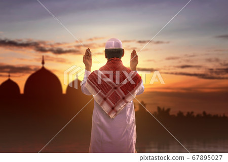 Rear view of Asian Muslim man standing while raised hands and praying Rear view of Asian Muslim man standing while raised hands and praying 67895027