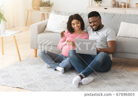 Expecting black family spending time together at home, using laptop 67896803
