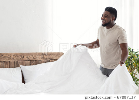 Happy black guy covering his bed with blanket 67897137