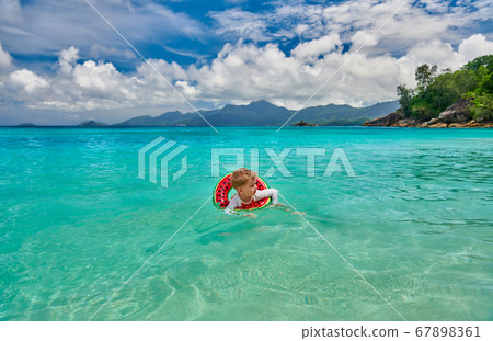Toddler boy on beach swimming with inflatable ring 67898361
