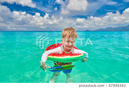 Toddler boy on beach swimming with inflatable ring 67898362