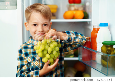 Little boy standing in front of open fridge and choosing food 67899431