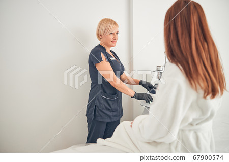 Cosmetologist showing her client special medical equipment 67900574