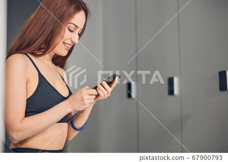 Sporty female with a gadget standing in a locker room 67900793