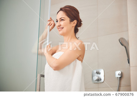 Contented lady standing in a shower booth 67900876