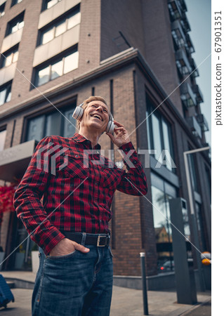 Joyful man in wireless headphones listening to music outdoors 67901351