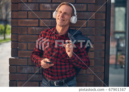 Cheerful man listening to music through wireless headphones outdoors 67901387