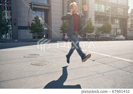Happy man talking on cellphone while walking and jumping on the street 67901432