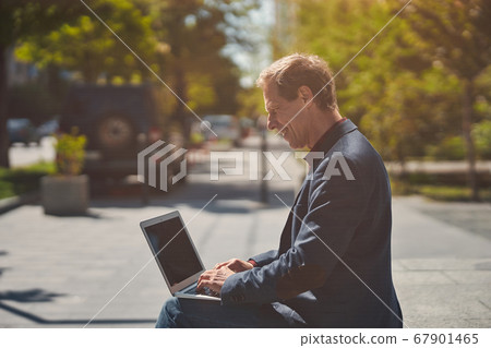Cheerful man working on laptop on sunny day Cheerful man working on laptop on sunny day 67901465