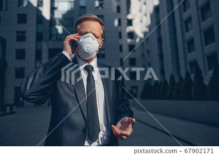 Well-dresses man in antiviral respirator talking on cellphone outdoors 67902171