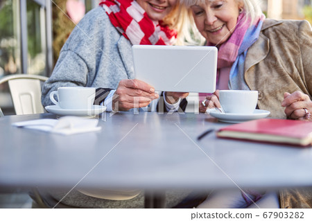 Adult woman showing photos on tablet for friend Adult woman showing photos on tablet for friend 67903282