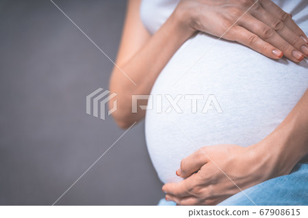 Pregnant woman holds hands on belly on a gray background. pregnancy, motherhood, people and 67908615