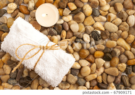 Sea stone natural pebble colorful background with towel and lighting candle close up top view Sea stone natural pebble colorful background with towel and lighting candle close up top view 67909171